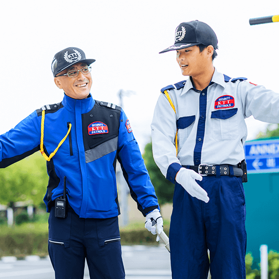 ベテランの教官が、若手警備員に駐車場警備のノウハウを現場で研修しているシーン