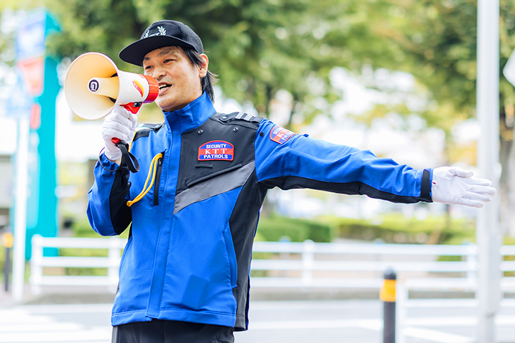 屋外で拡声器をもった警備員が、イベント来場者を会場へ誘導している様子
