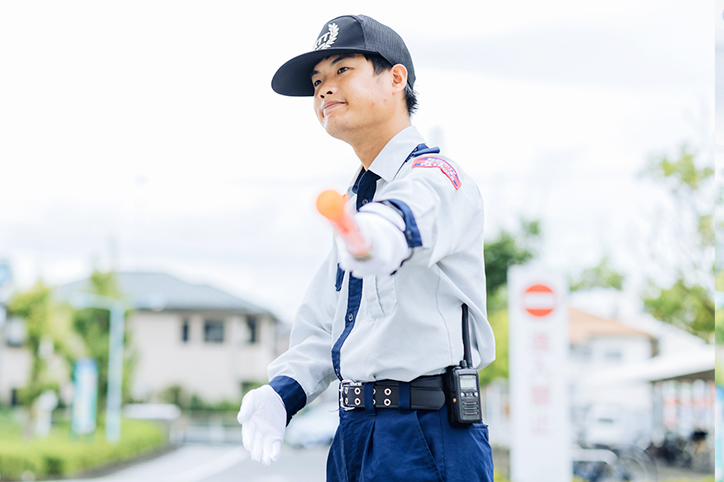 屋外の駐車場で、警備員が車を誘導している様子
